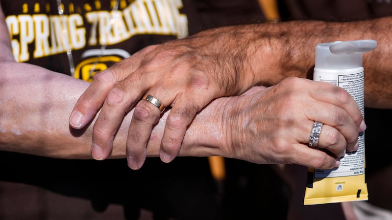 FILE - A man applies sunscreen to a woman's arm before a spring training baseball game between...
